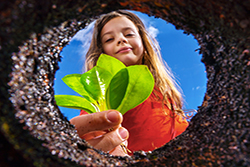Young girl holding plant with soil background.
