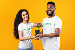Two volunteers holding a plant with an orange background.