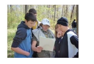 Teenagers looking at study material in a forest.