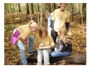 Young girls sitting on a tree log taking notes.
