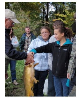Young girl holding a big fish with onlookers in background.